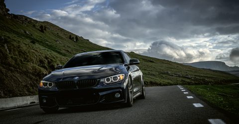 Black BMW M4 driving through countryside with cliffs in the background on a cloudy day