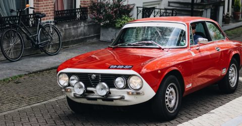 Red Alfa Romeo driving through streets near to houses