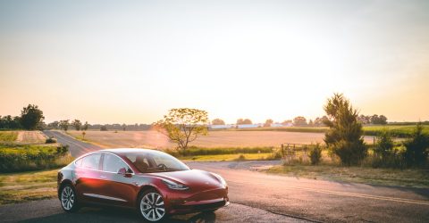 Red Tesla Electric Vehicle parked in the countryside with sun