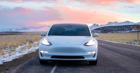 White Tesla Electric Vehicle driving in scenic route with mountains